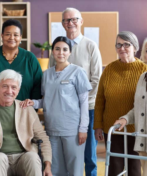 Diverse group of senior people looking at camera in retirement home while posing with nurse all smiling